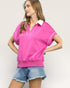 Woman wearing a pink blouse with white trim and denim shorts on a plain background