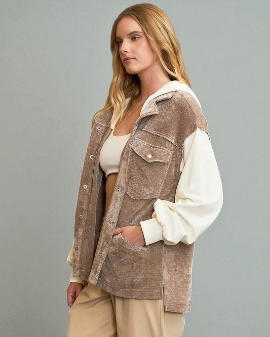 Woman wearing a brown corduroy vest over a white shirt and beige pants on a gray background