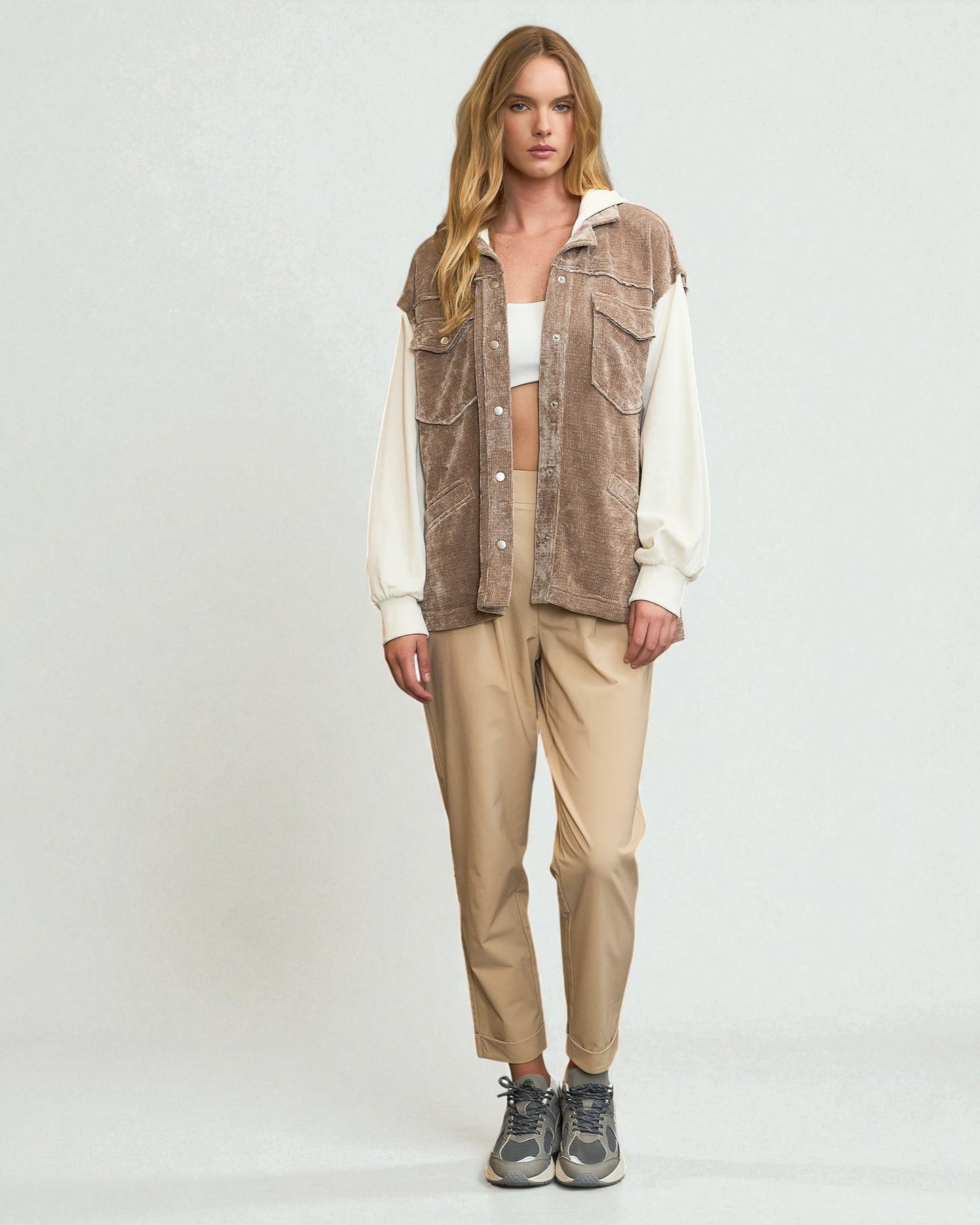 Woman wearing a brown vest over a white shirt with beige pants on a white background