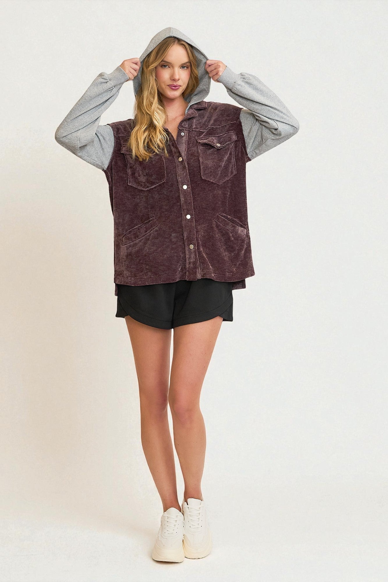 Woman wearing a purple vest over a gray hoodie with black shorts on a white background