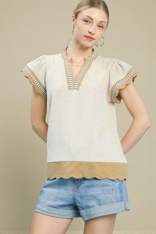 Woman wearing a beige top with striped trim and denim shorts on a beige background