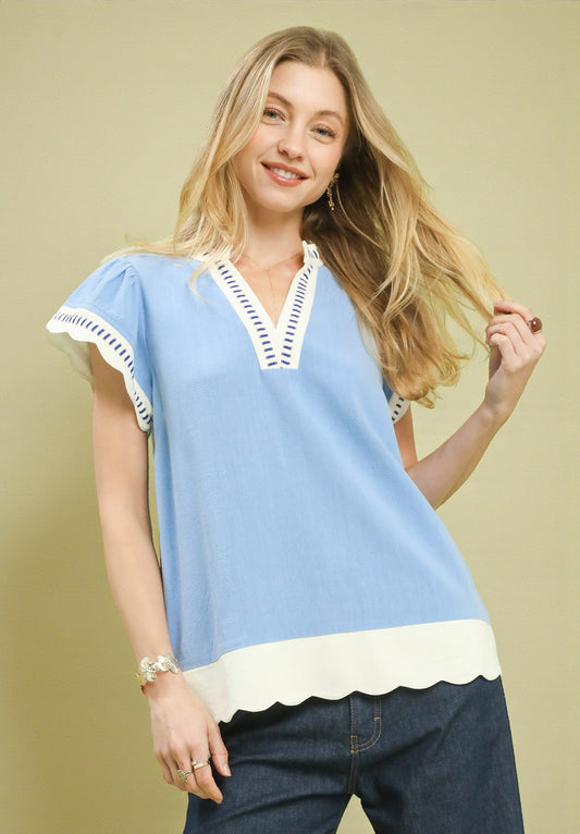 Woman wearing a light blue blouse with white trim against a beige background