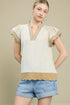 Woman wearing a beige top with striped trim and denim shorts on a beige background
