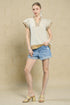 Woman wearing a beige top and denim shorts against a beige wall.