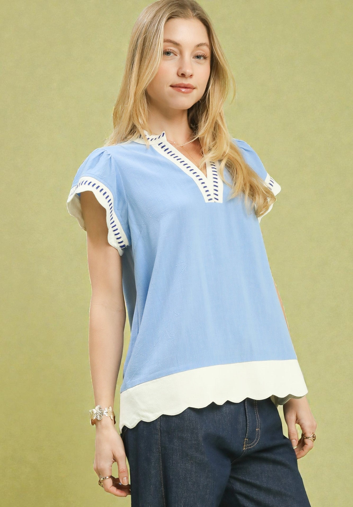 Woman wearing a light blue blouse with white trim against a green background