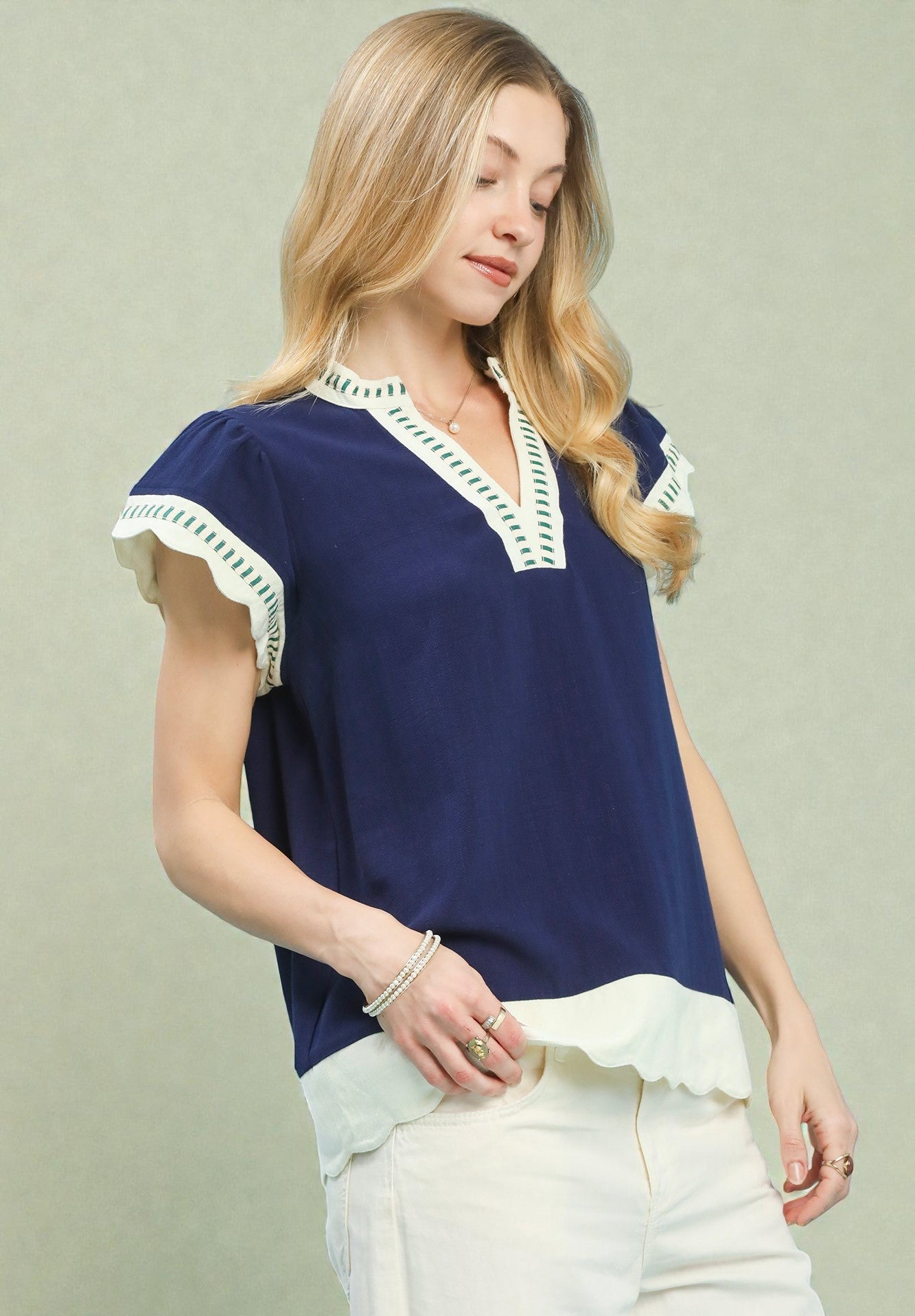 Woman wearing a navy blue top with white trim on a light green background