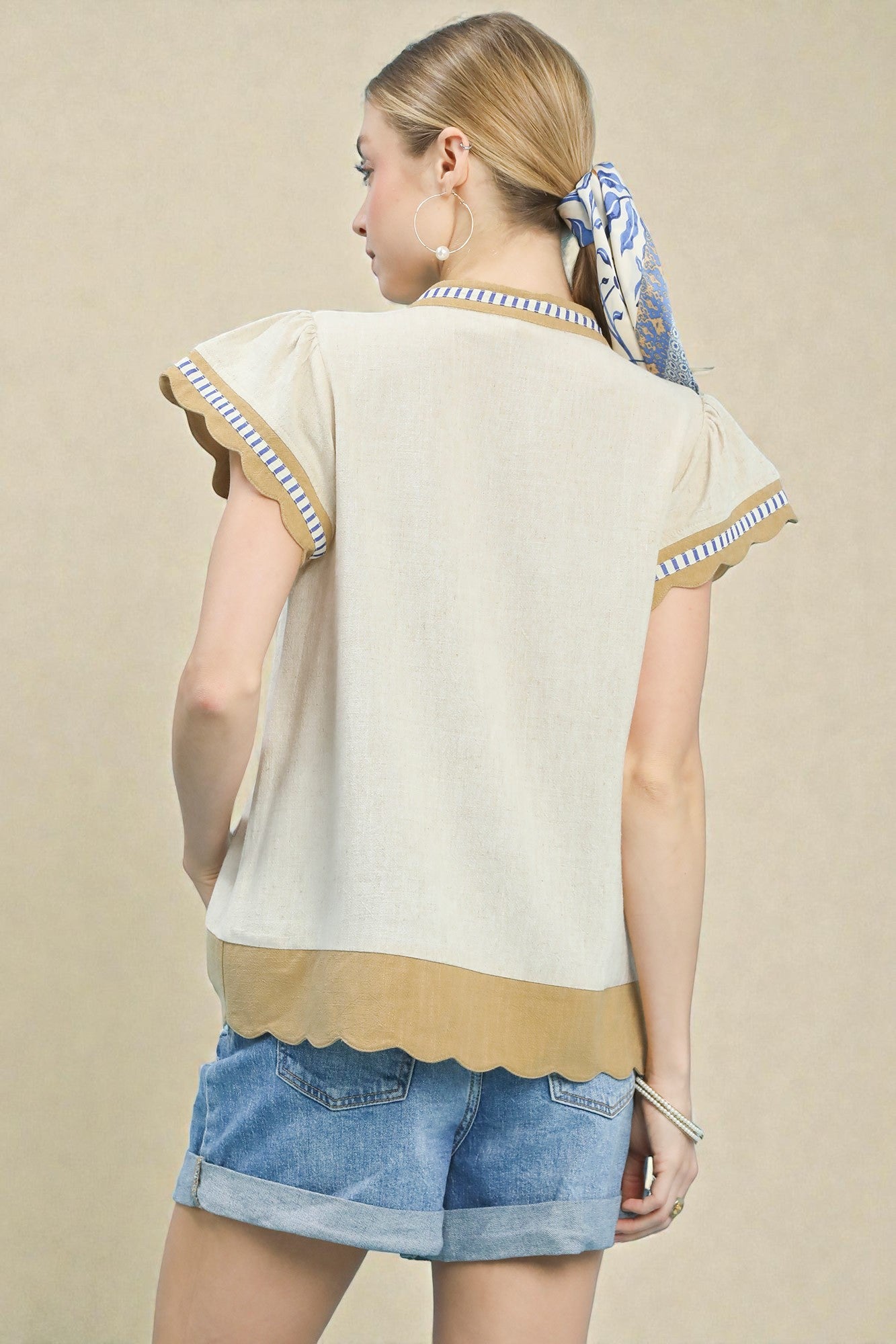 Woman wearing a beige top with ruffled sleeves and denim shorts on a beige background