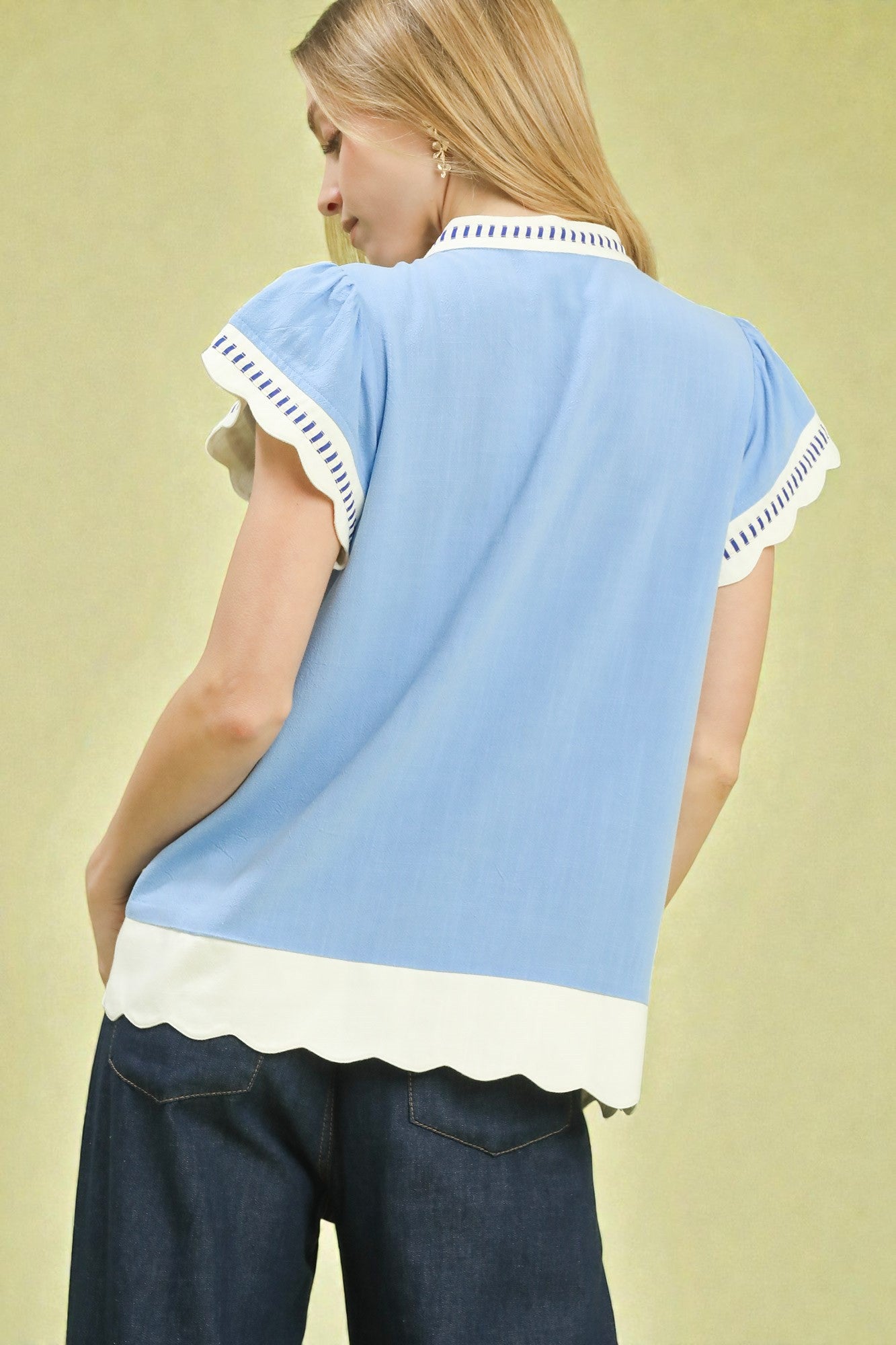 Woman wearing a light blue top with white trim on a beige background