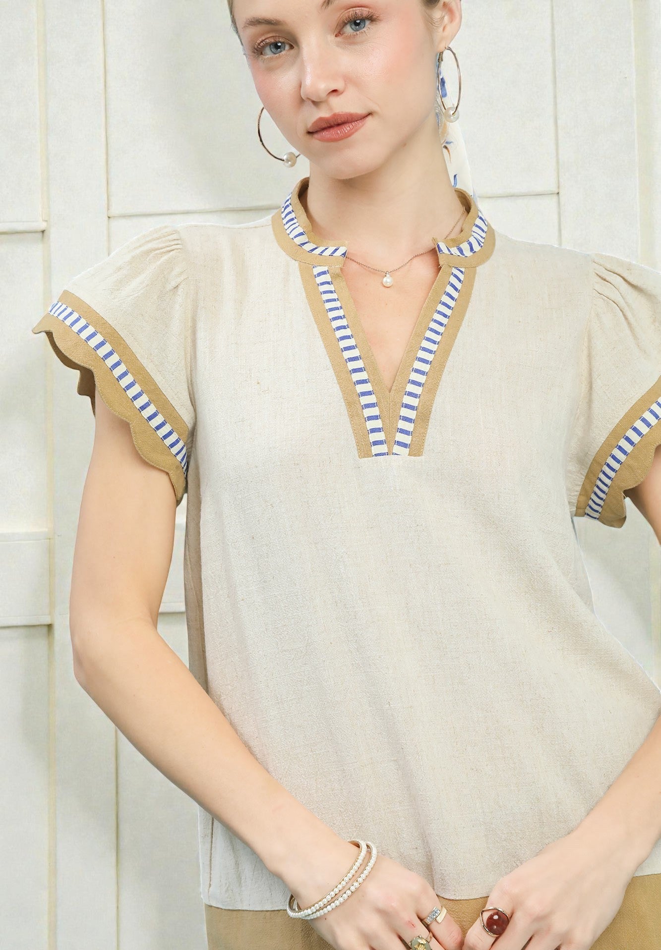 Woman wearing a beige blouse with striped trim against a white background