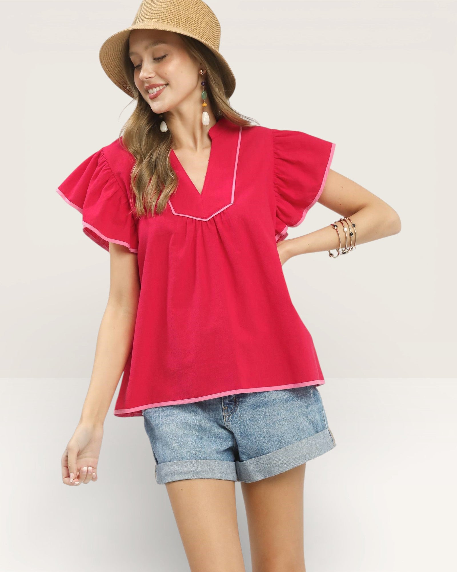 Woman wearing a red blouse with ruffled sleeves and denim shorts on a plain background