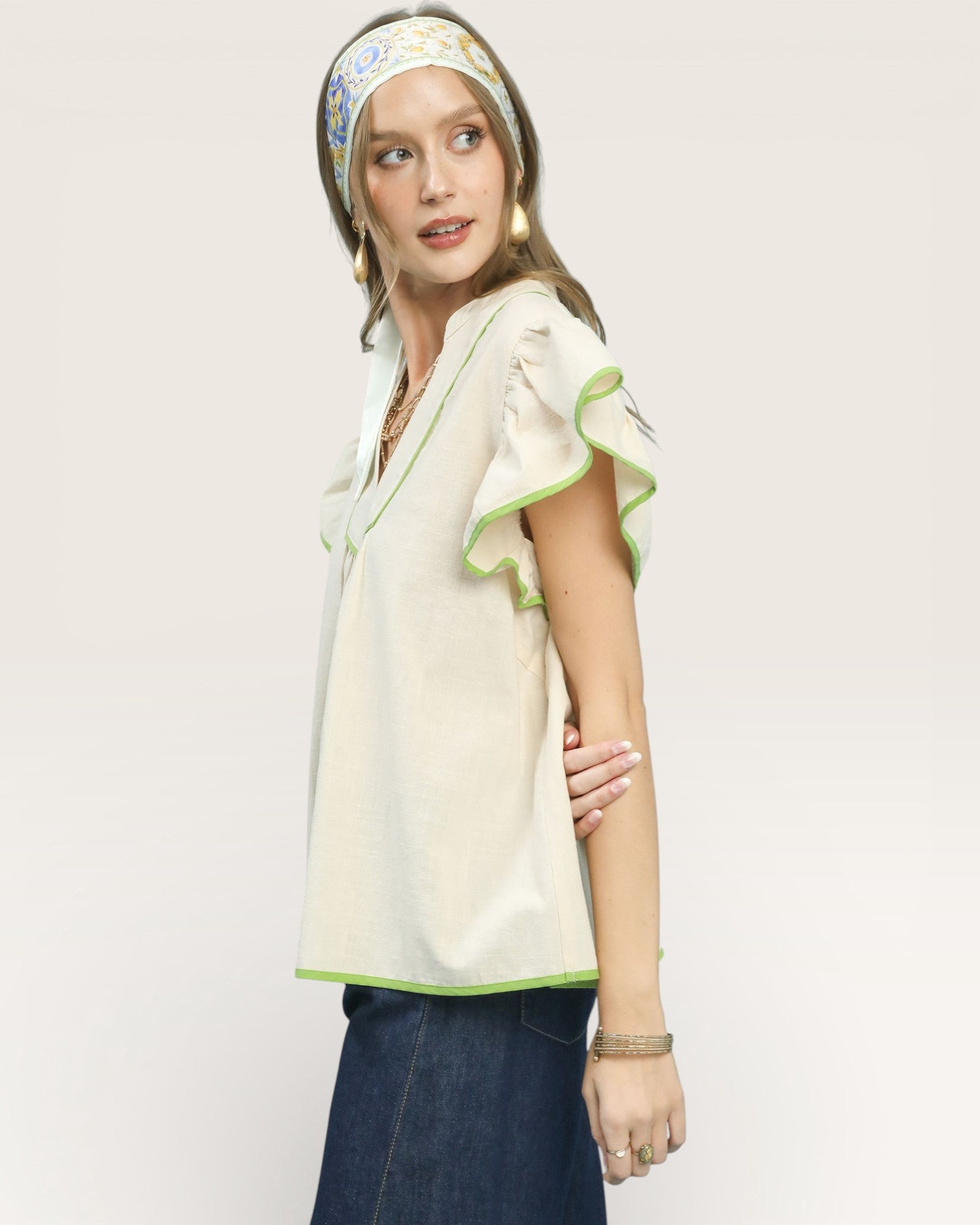 Woman wearing a light-colored blouse with green trim and a headscarf on a plain background