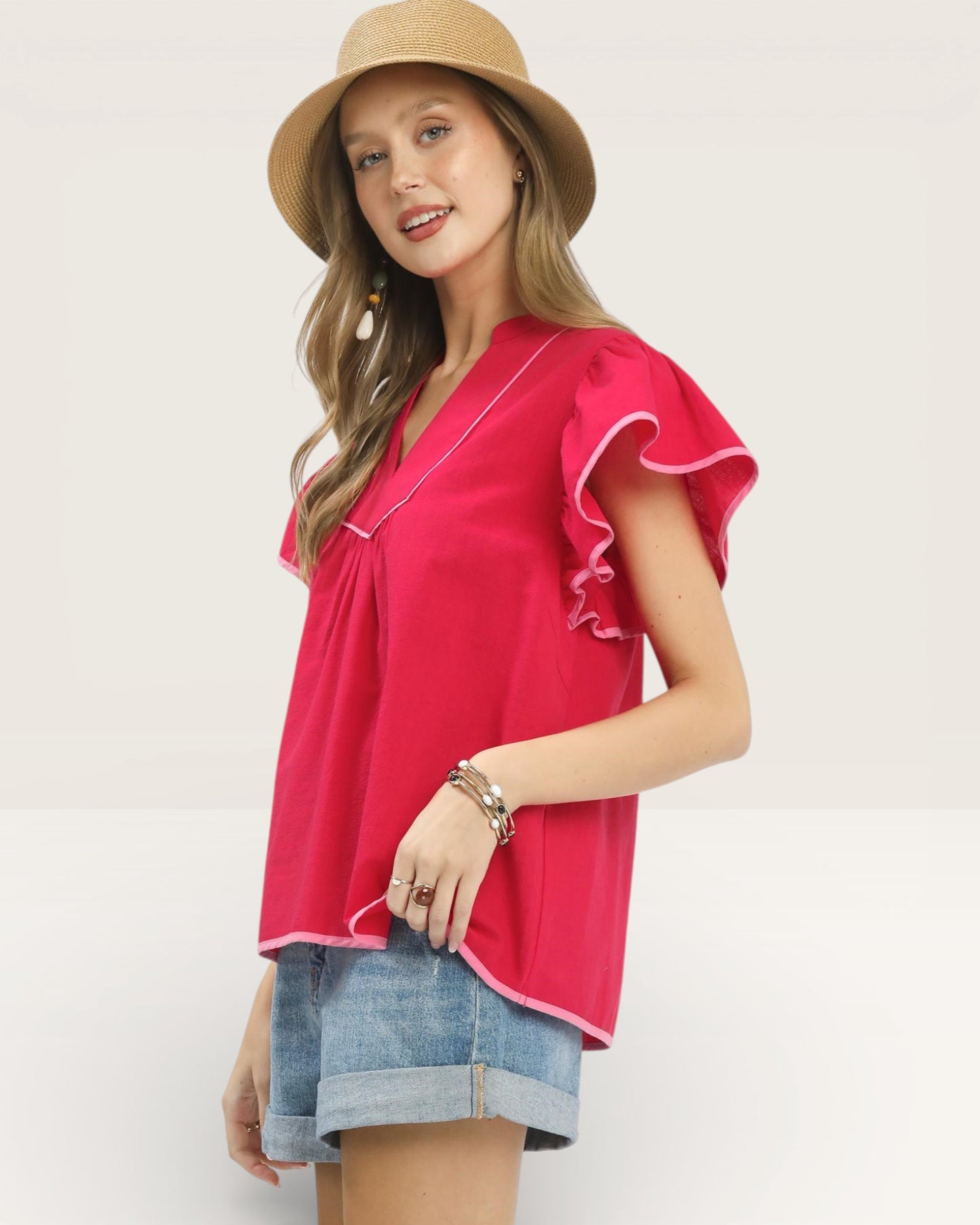 Woman wearing a pink blouse with ruffled sleeves and a beige hat on a white background
