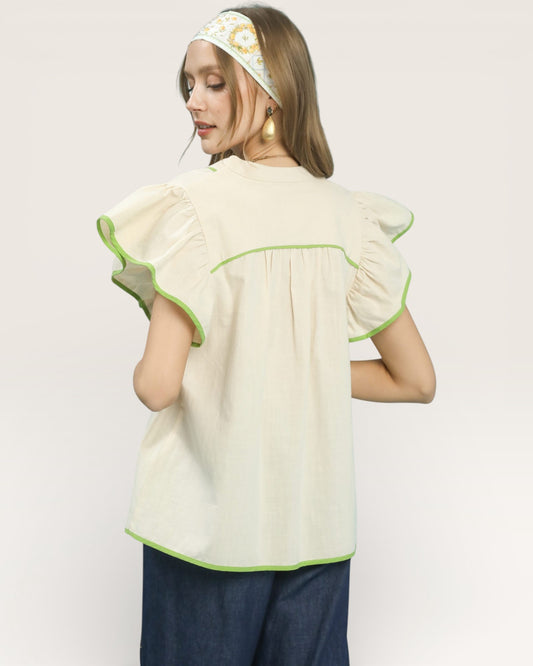 Woman wearing a cream blouse with green trim on a plain background