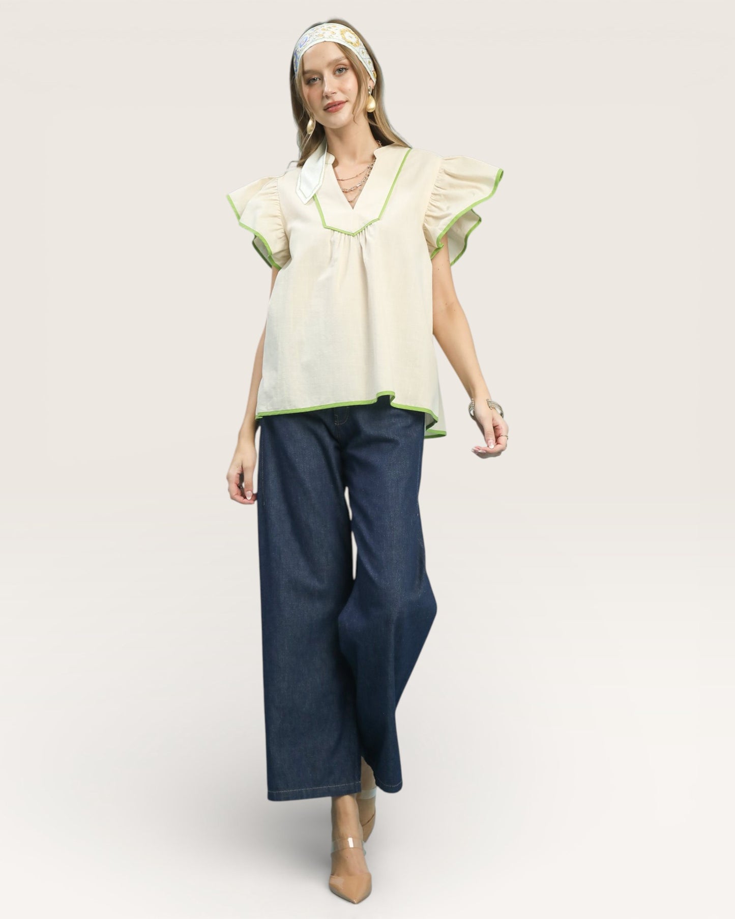 Woman wearing a light-colored blouse with ruffled sleeves and dark blue jeans on a white background