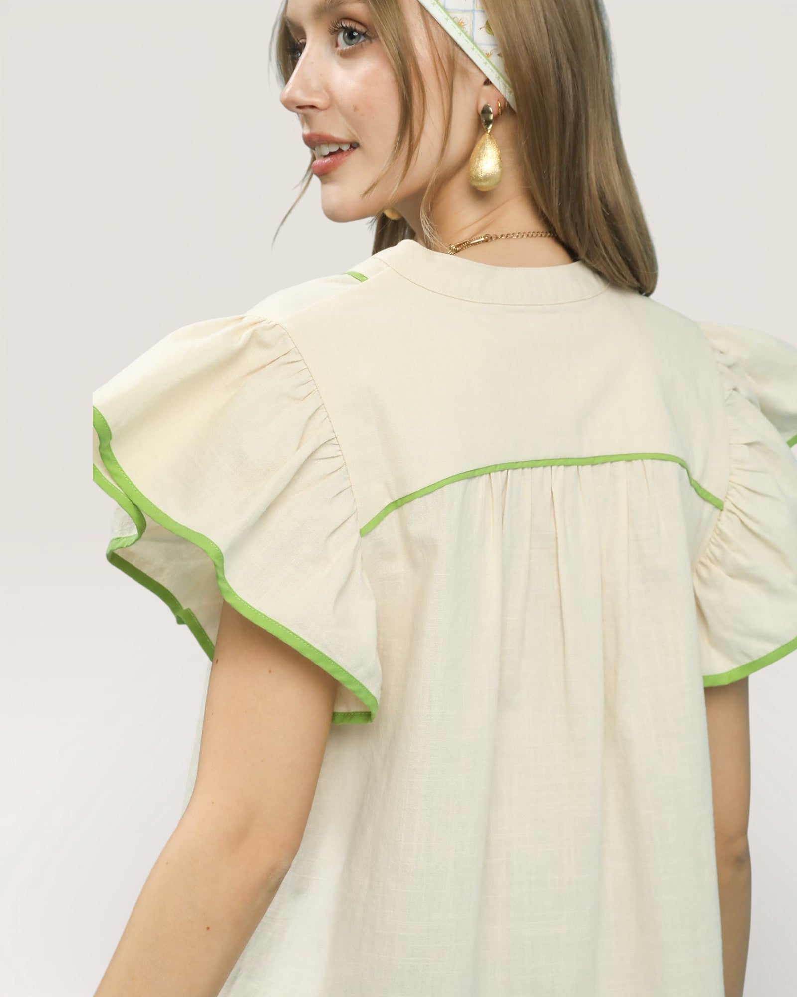 Woman wearing a light-colored blouse with green trim on a plain background