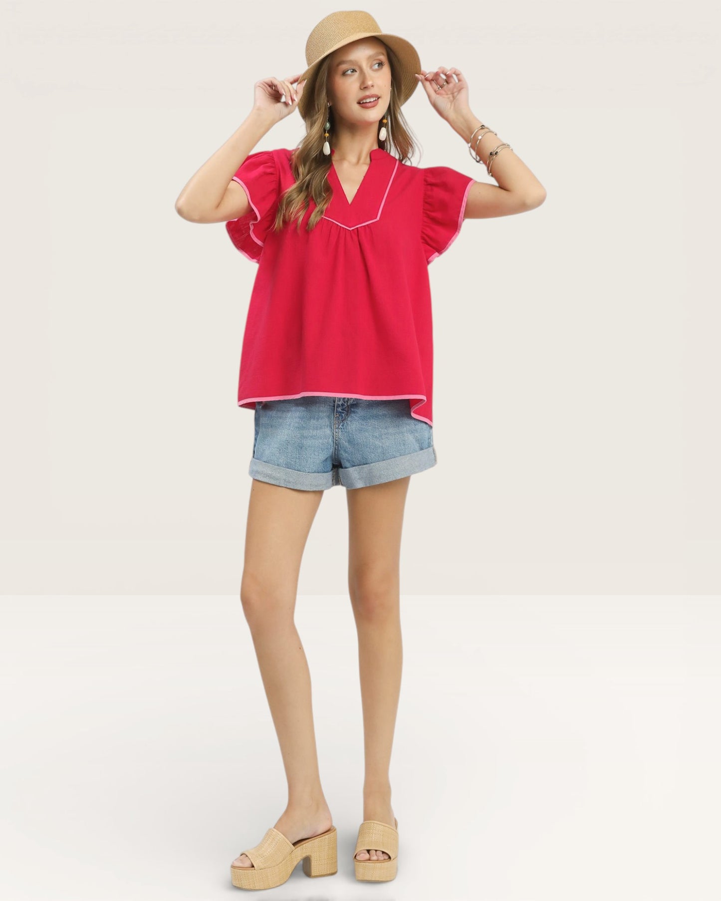 Woman wearing a red blouse, denim shorts, and a beige hat on a light background