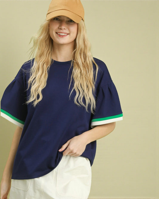 Woman wearing a navy blue shirt with green and white trim and a beige cap on a beige background