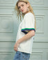 Woman wearing a white t-shirt with colorful accents against a light gray wall.