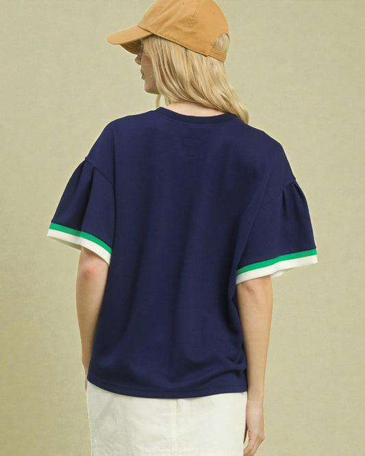 Person wearing a navy blue t-shirt with green and white trim on a beige background