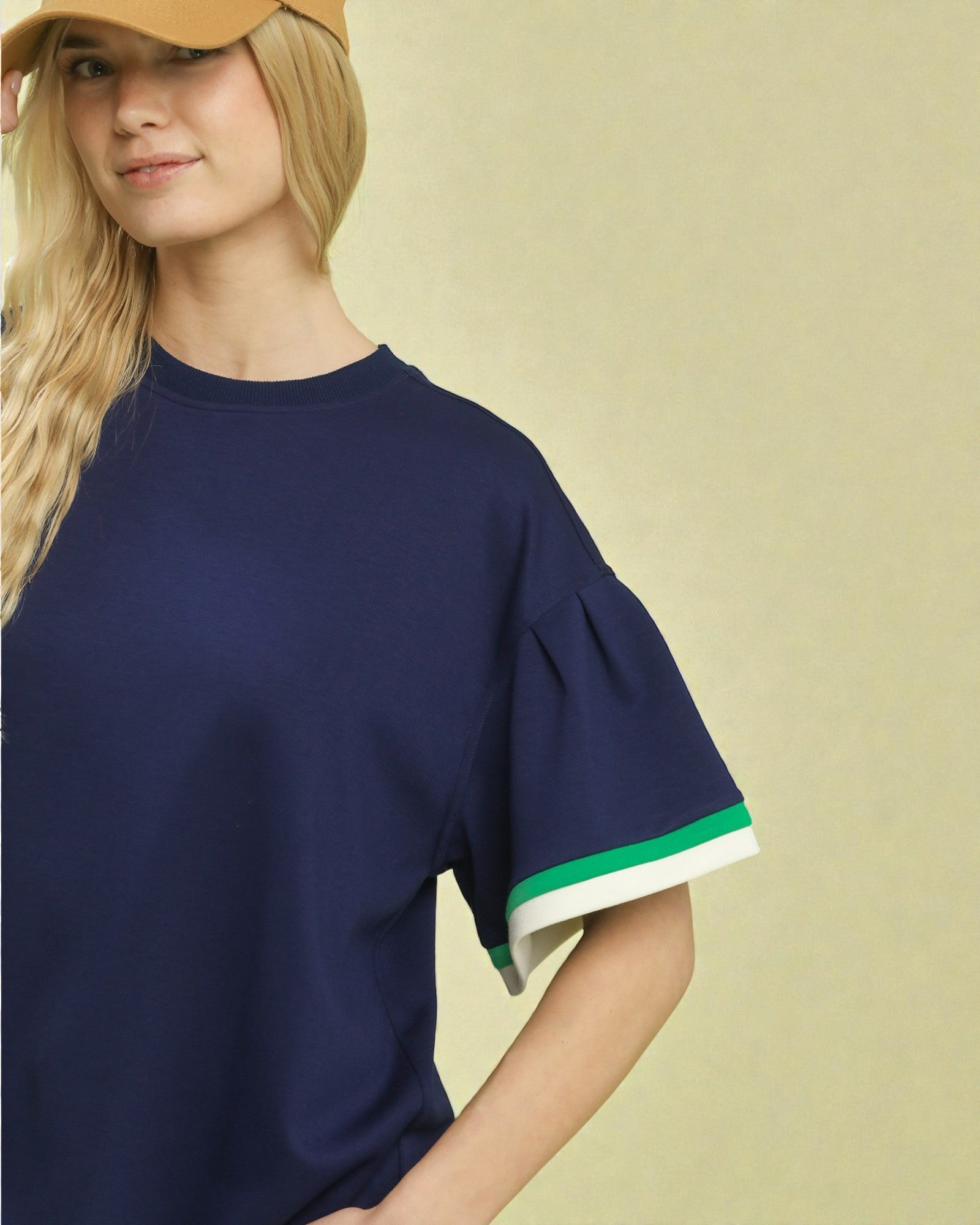 Woman wearing a navy blue top with green trim on a beige background