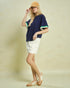 Woman wearing a navy blue top, white shorts, and a beige cap on a beige background