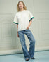Woman wearing a white oversized shirt with colorful trim and blue jeans in a minimalistic setting.