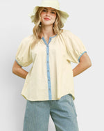 Woman wearing a yellow blouse with blue trim and striped pants on a light gray background