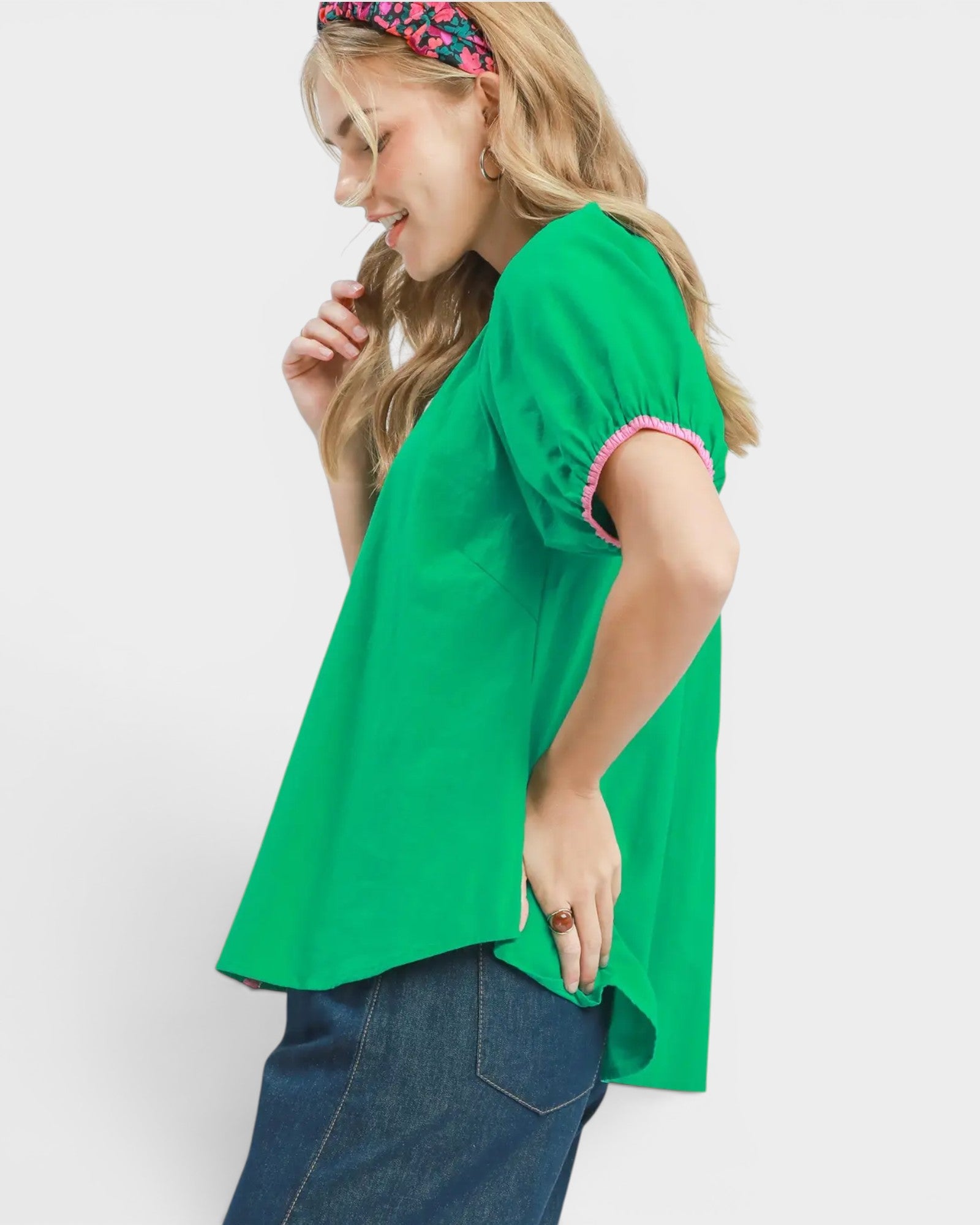 Woman wearing a green blouse with pink trim and blue jeans on a white background