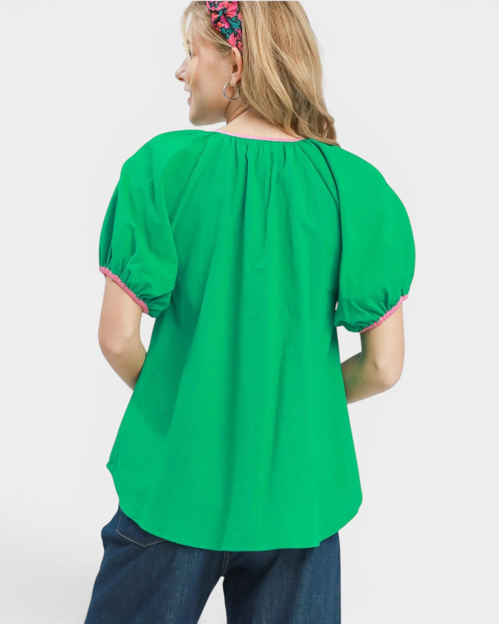 Green blouse with pink trim worn by a person on a white background