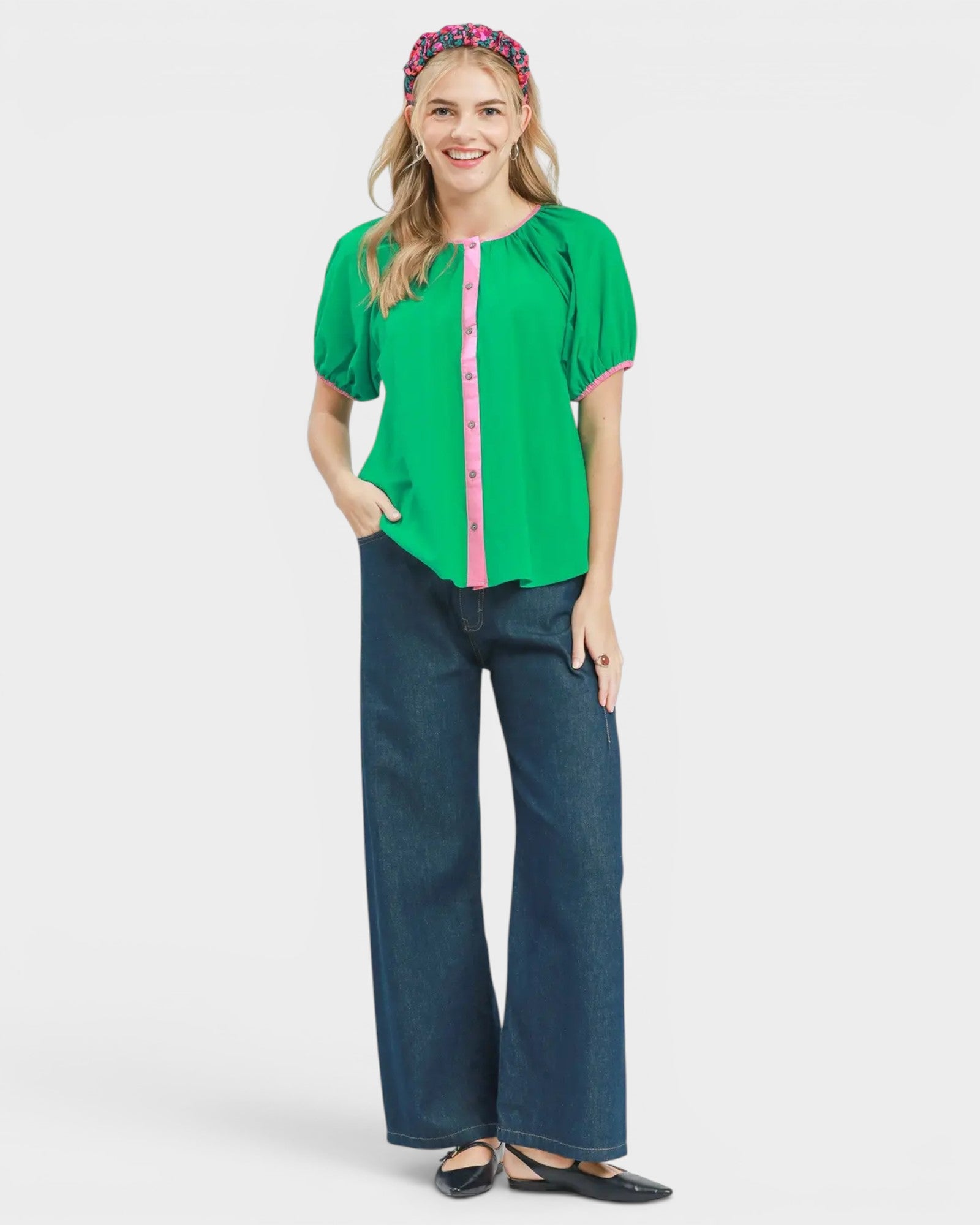 Woman wearing a green blouse with pink accents and blue jeans on a white background