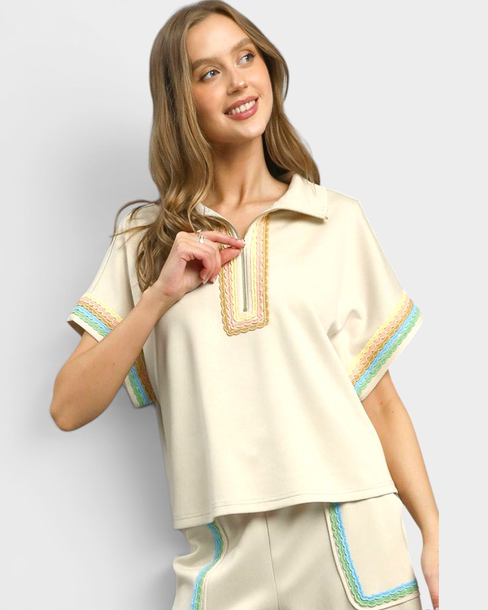Woman wearing a cream-colored outfit with decorative trim on a plain background