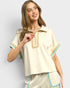 Woman wearing a cream-colored outfit with decorative trim on a plain background