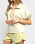 Woman wearing a beige top with colorful trim and light yellow shorts on a white background