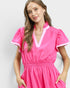 Woman wearing a bright pink dress with white trim on a plain background
