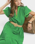 Woman wearing a green dress with a beige belt, sitting against a white background.