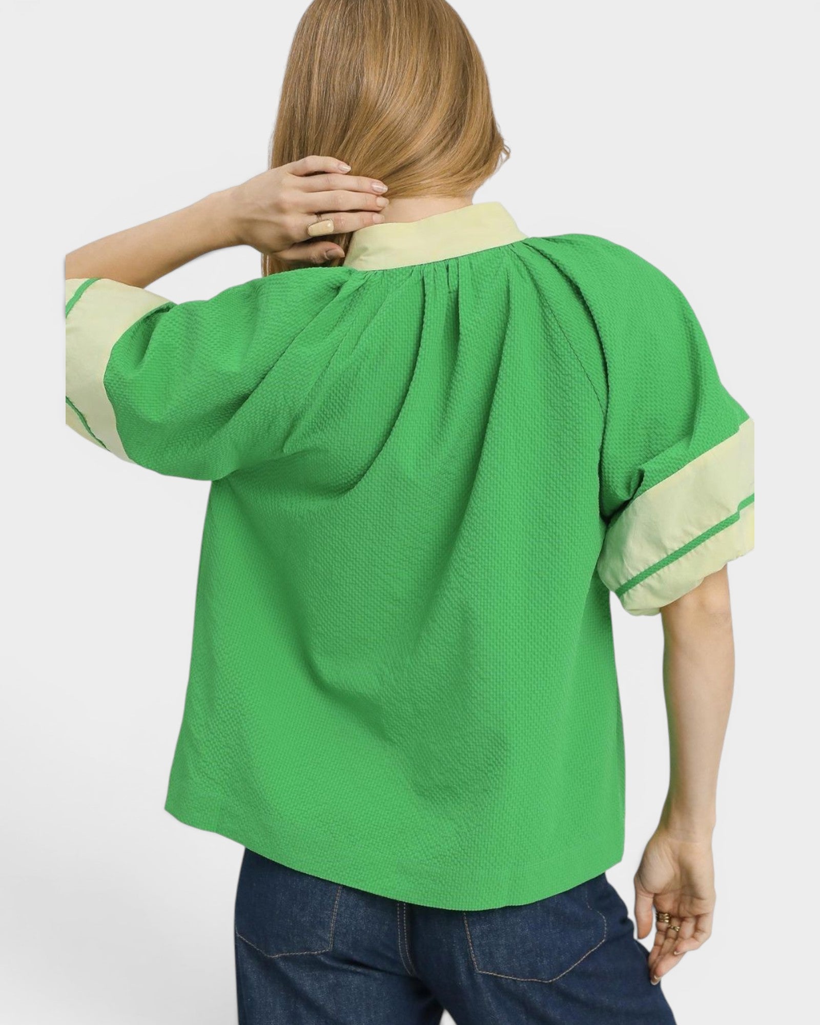 Green blouse with beige accents worn by a person on a white background