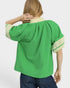 Green blouse with beige accents worn by a person on a white background