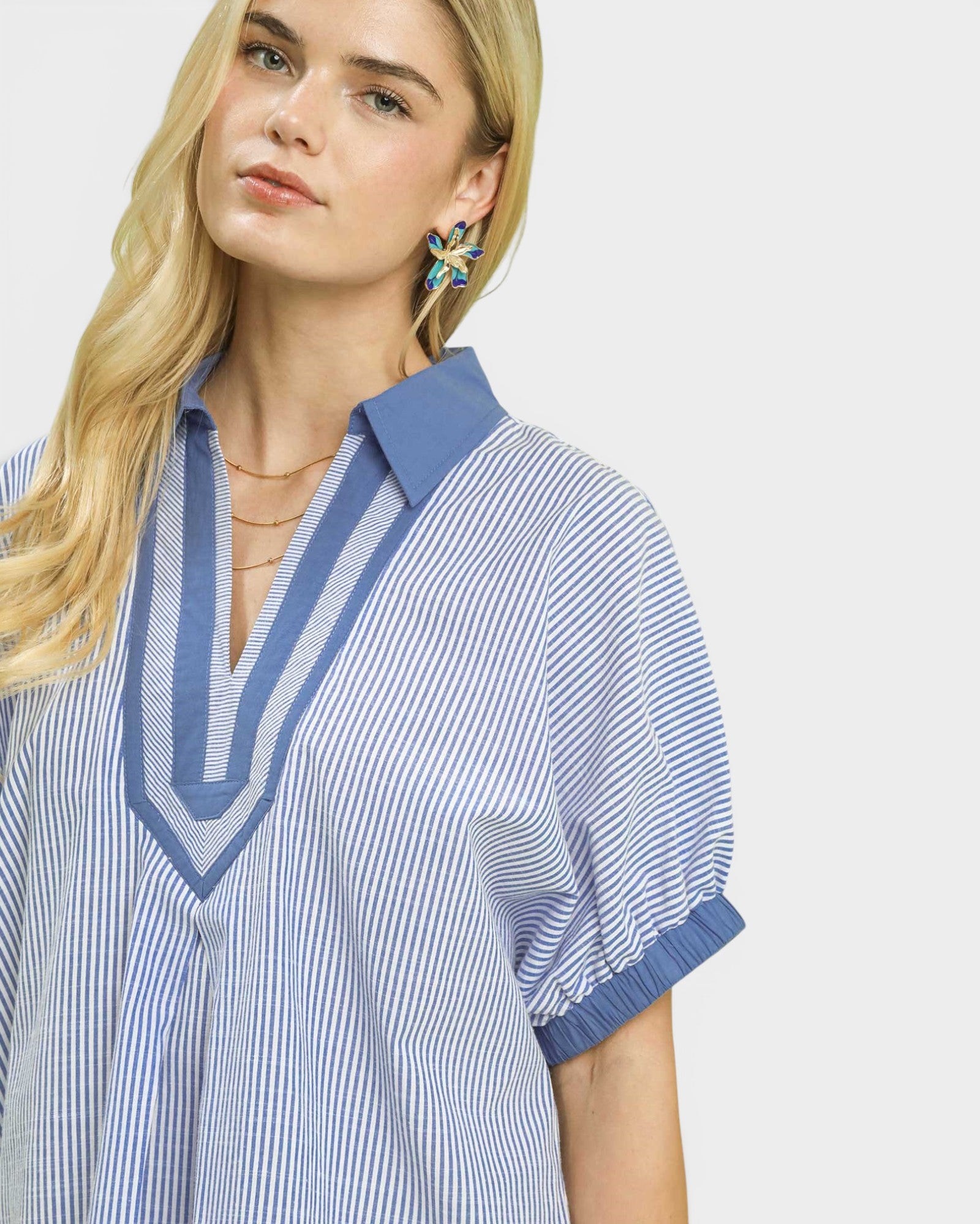 Woman wearing a blue and white striped shirt with a blue collar on a light gray background