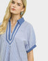 Woman wearing a blue and white striped shirt with a blue collar on a light gray background