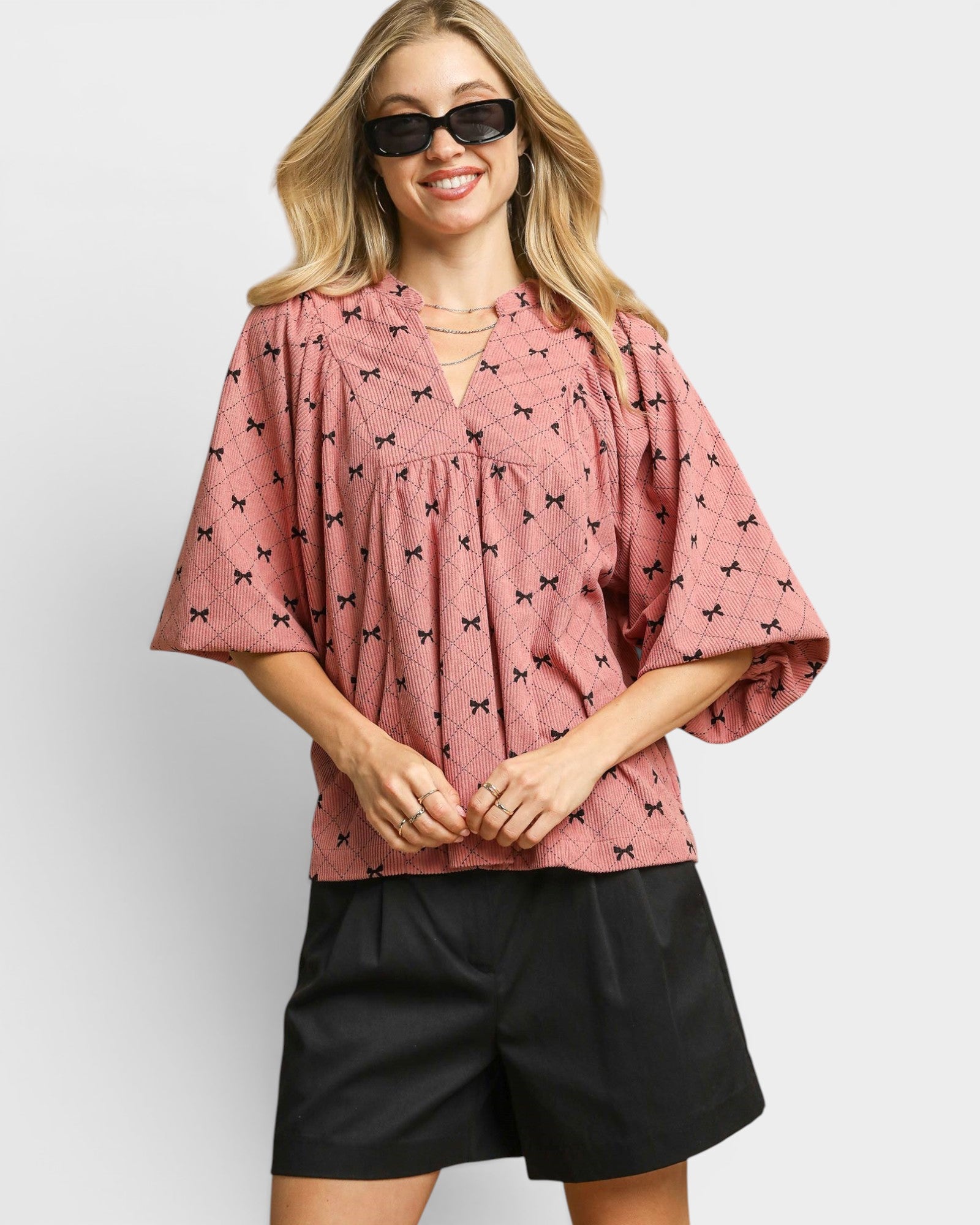 Woman wearing a pink blouse with black patterns and black shorts on a white background