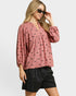 Woman wearing a pink blouse with black patterns and black shorts on a white background