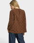 Woman wearing a brown blouse with black patterns on a white background