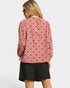 Person wearing a pink blouse with black patterns and black shorts on a white background