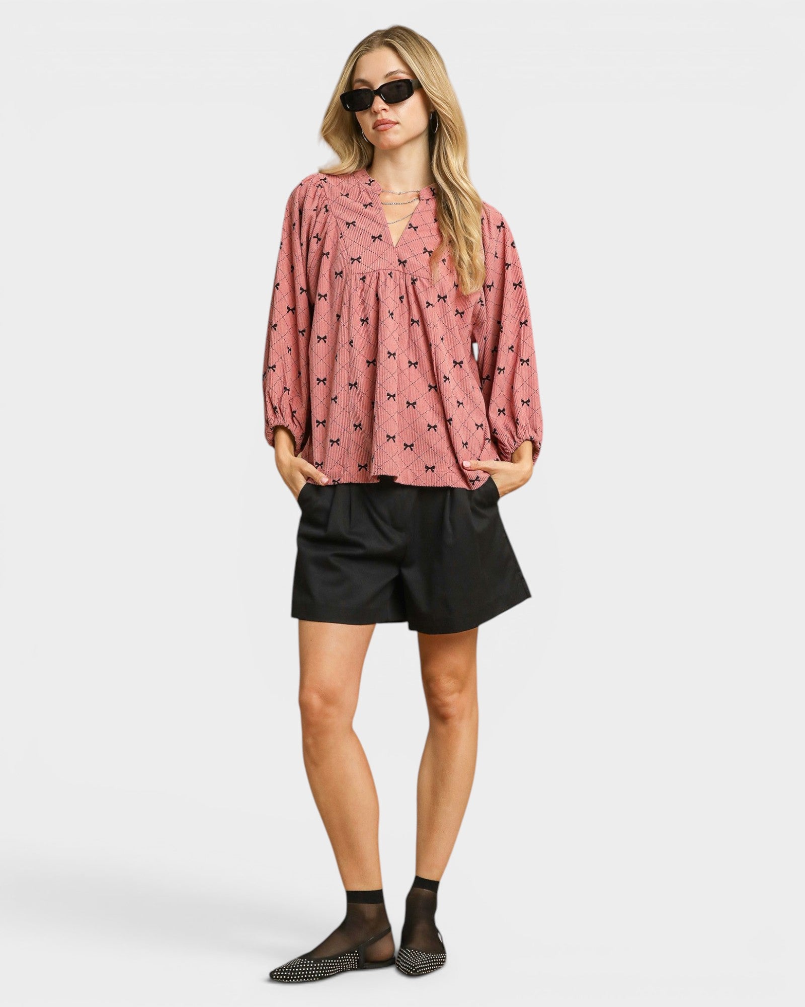 Woman wearing a pink blouse with black patterns and black shorts on a white background