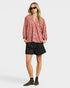 Woman wearing a pink blouse with black patterns and black shorts on a white background