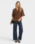 Woman wearing a brown patterned blouse and blue jeans on a white background