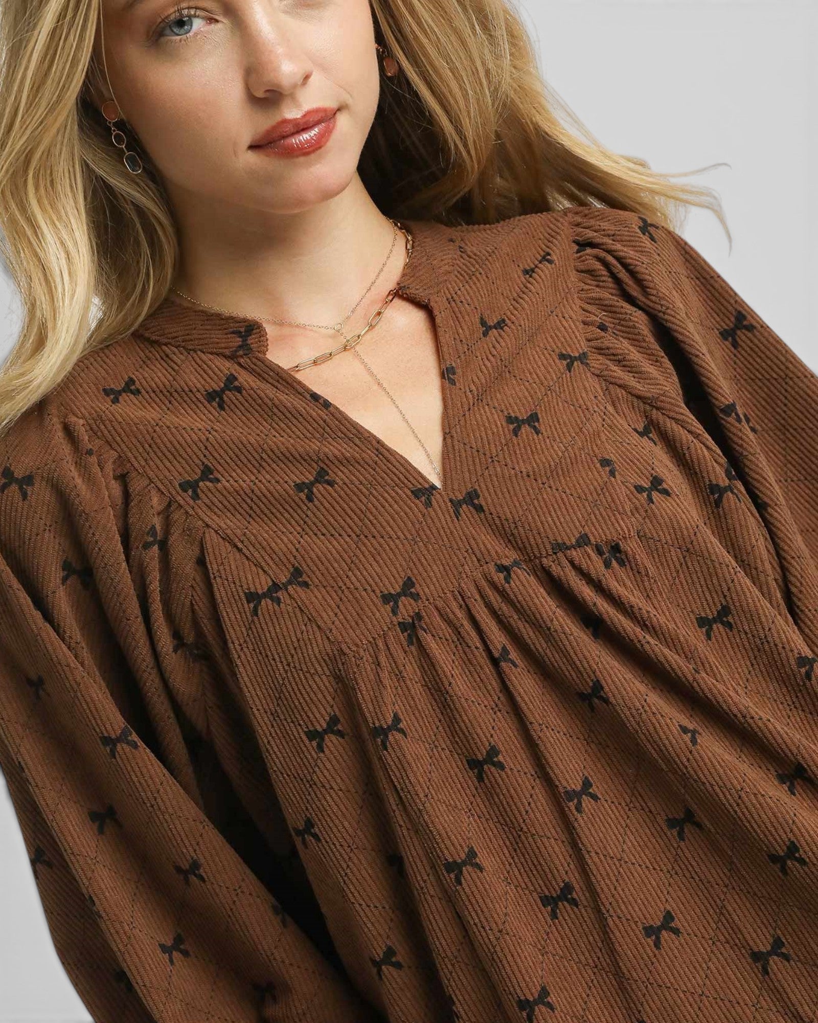 Woman wearing a brown dress with black bow patterns against a neutral background