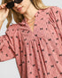 Woman wearing a pink blouse with black bow pattern against a light background