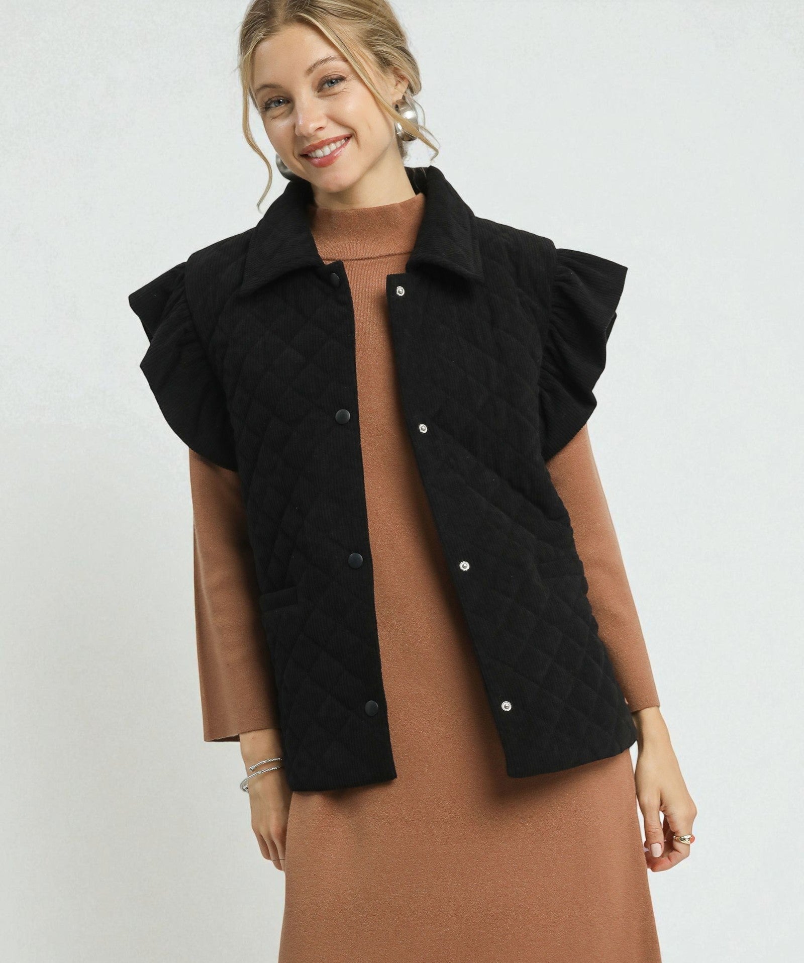 Woman wearing a black quilted vest over a brown dress on a light gray background