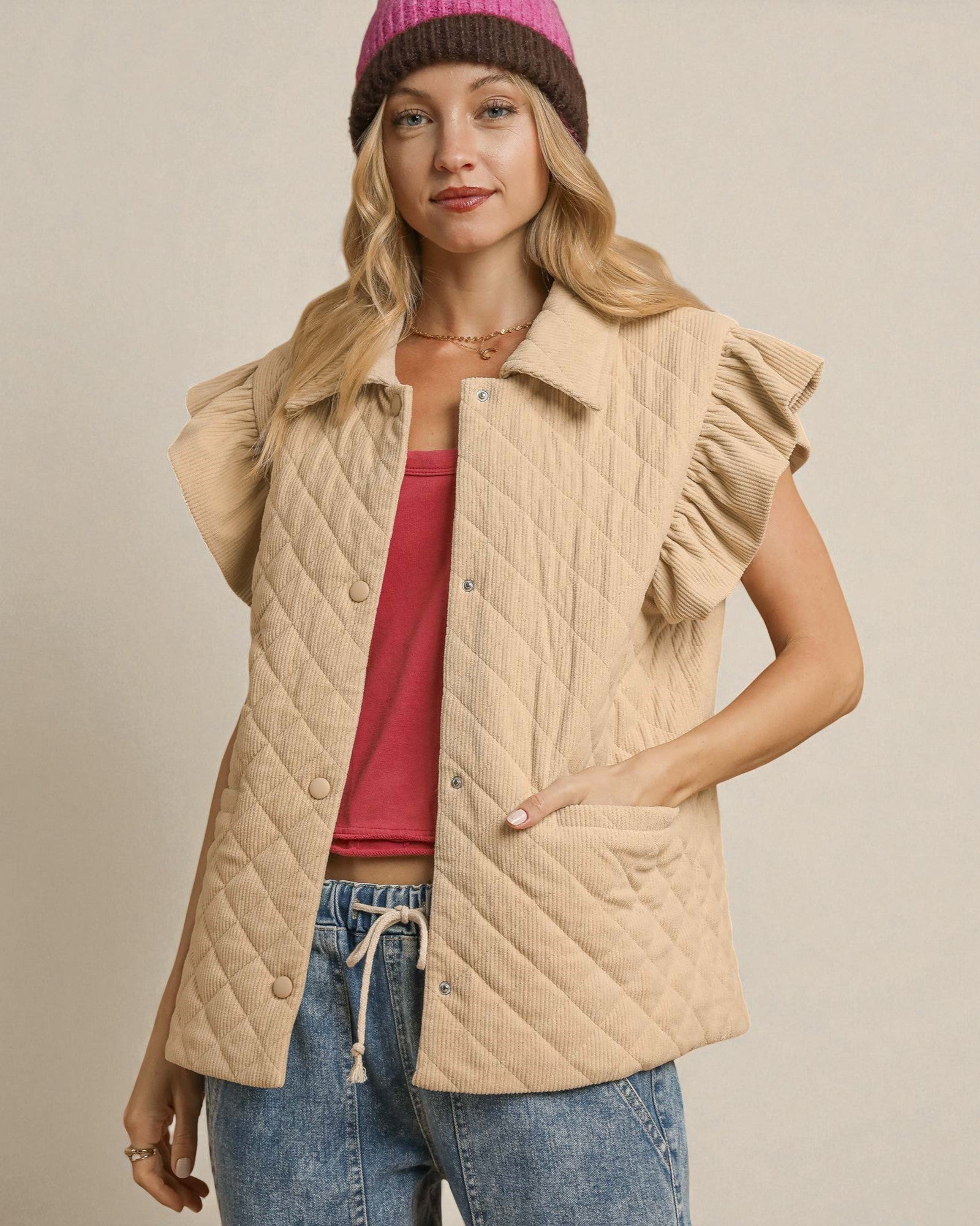 Woman wearing a beige quilted vest over a red top and blue jeans, with a neutral background.